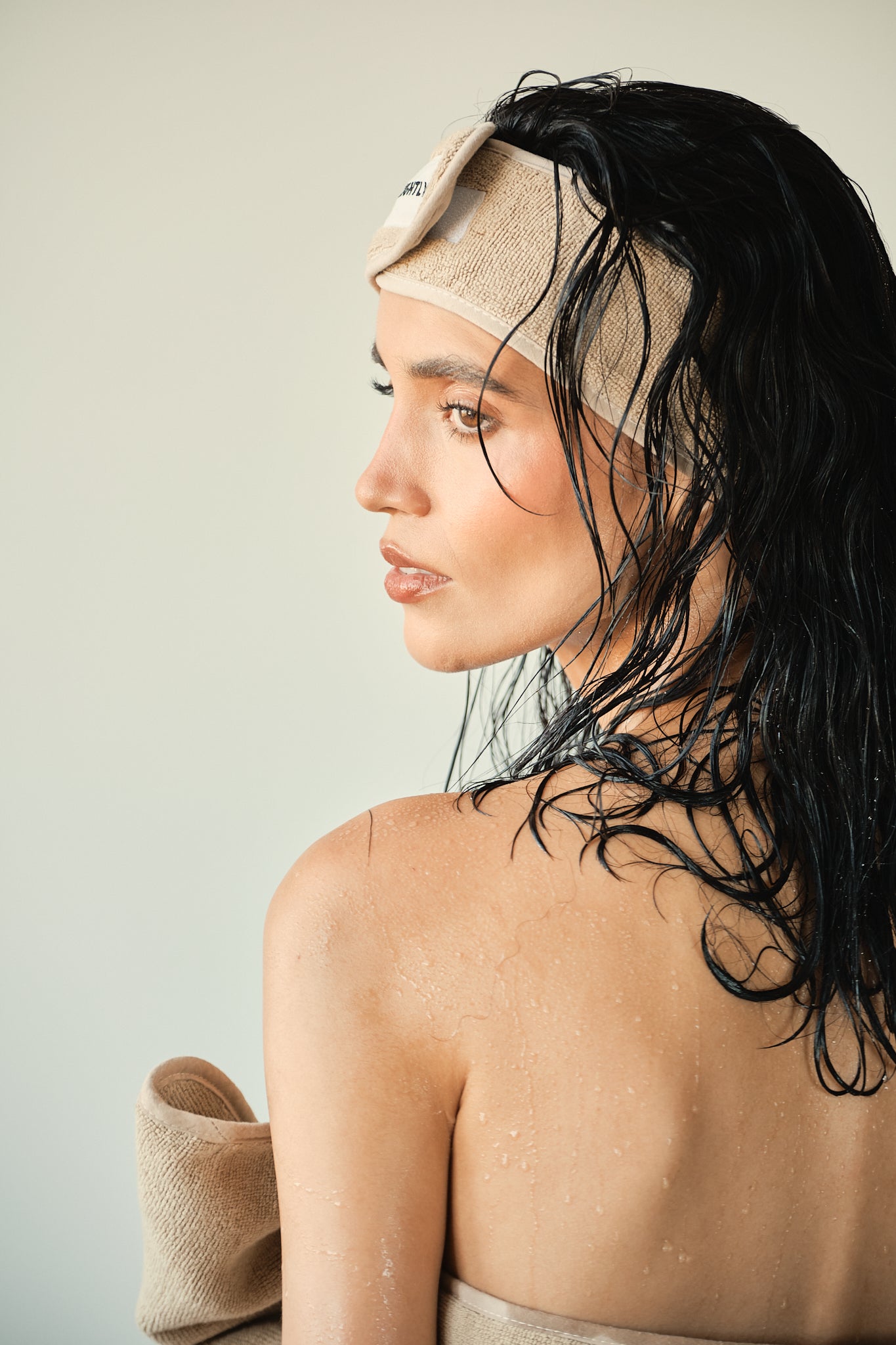 Woman with wet hair wearing a beige headband against a neutral background